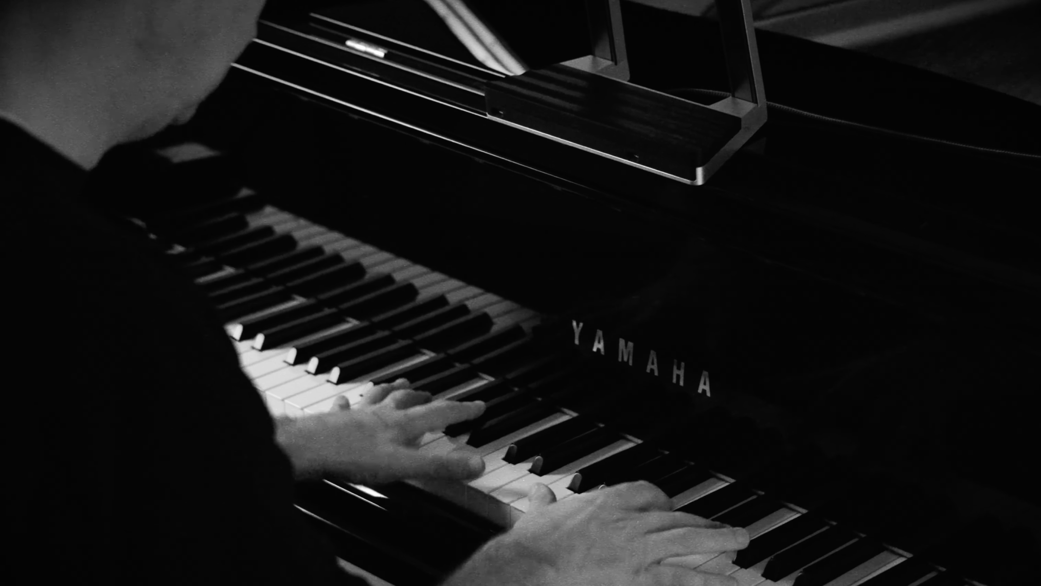 A person playing a Yamaha piano, with both hands on the black and white keys in a dimly lit setting.
