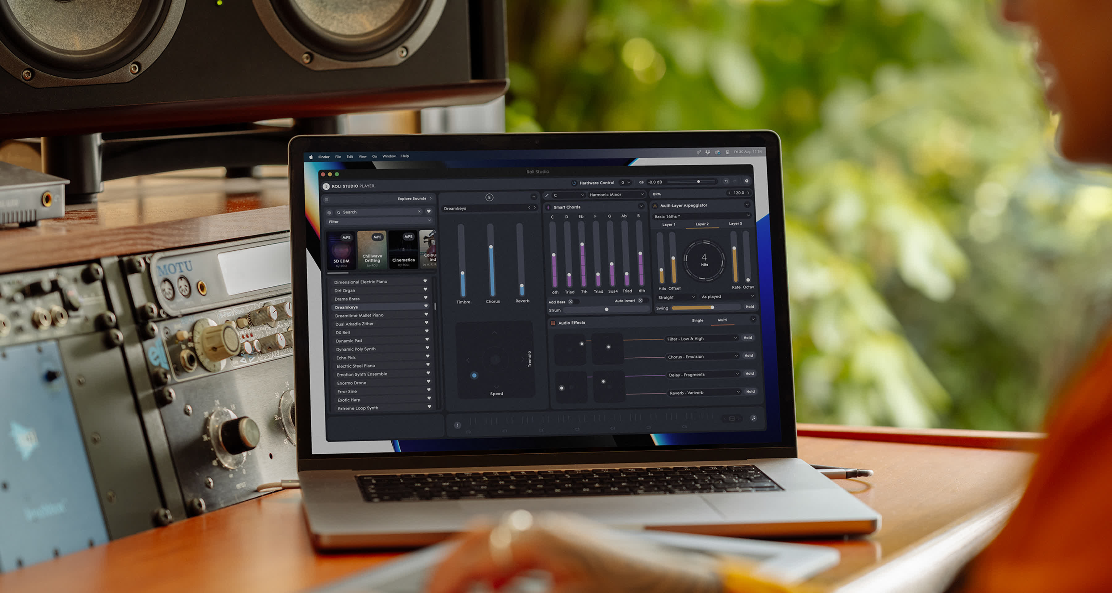 A person using a laptop on a wooden desk in a studio setting, with the ROLI Studio software open on the screen and audio equipment visible in the background.