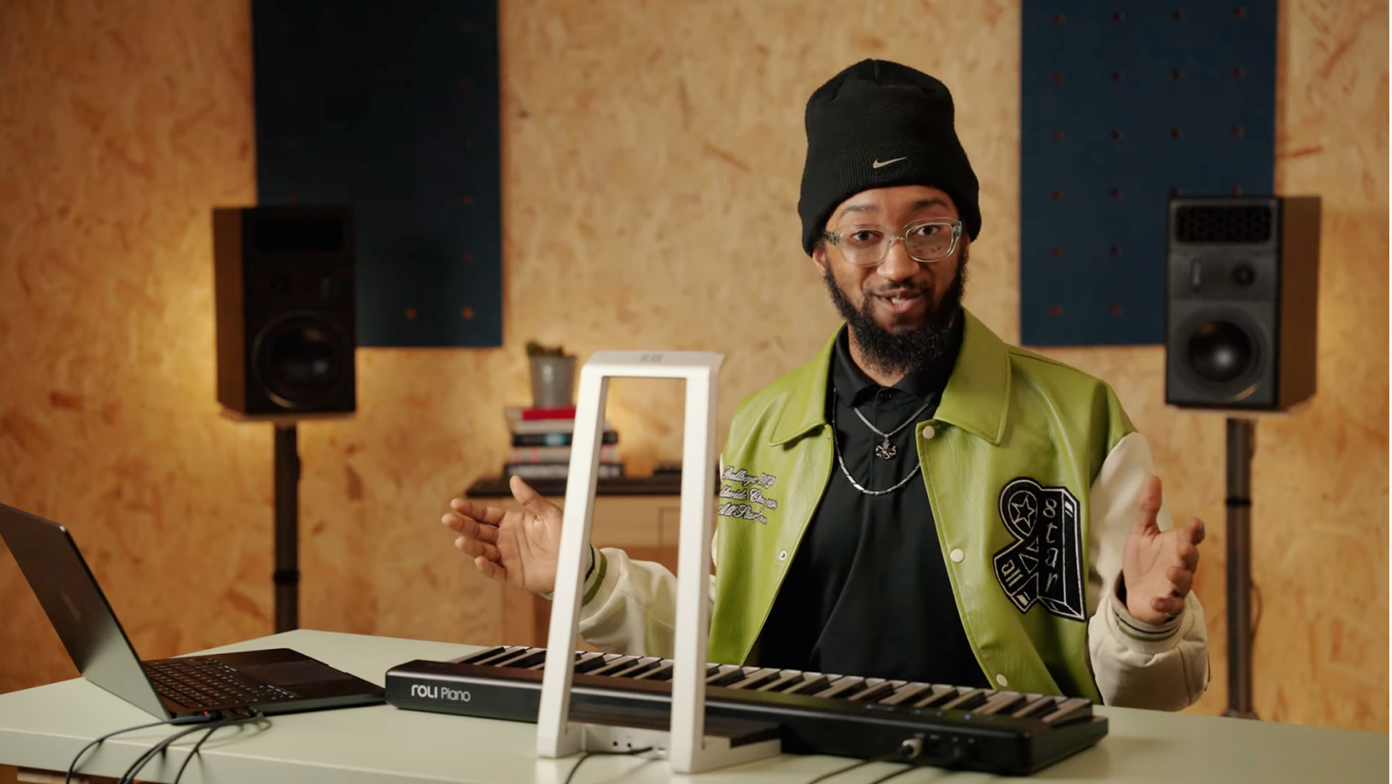 A person sitting at a desk in a studio setting, with a ROLI Piano keyboard connected to a laptop and a rectangular white frame positioned above the instrument.