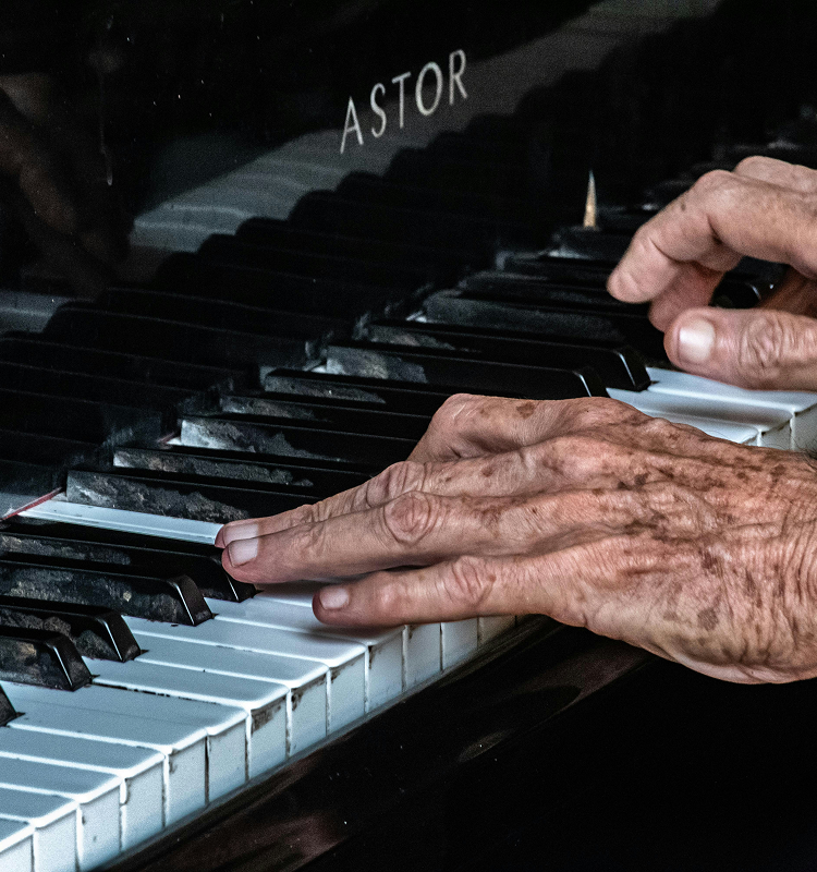 Close-up of two hands playing an acoustic piano with the brand name "Astor" visible above the black and white keys.