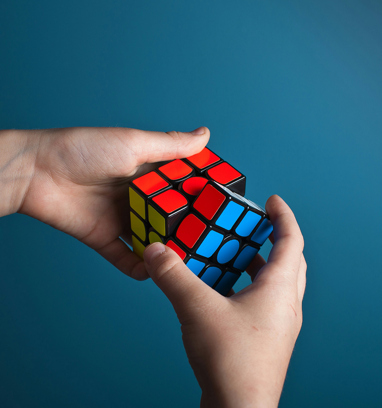 Two hands twisting a colorful Rubik's Cube puzzle against a plain blue background.